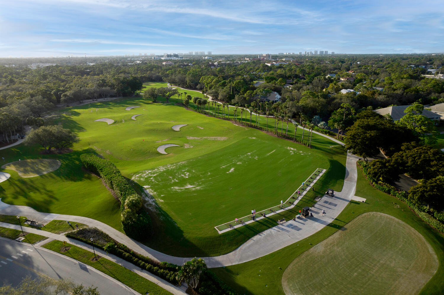 Aerial view of a Naples golf driving range with sand bunkers, manicured greens, and nearby residences.